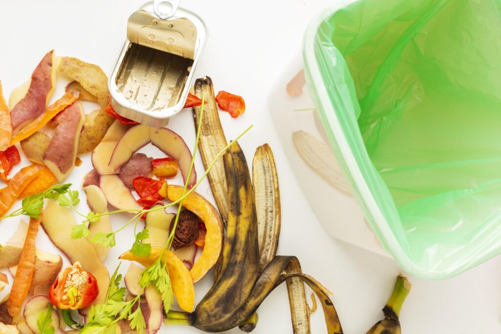 Een vuilnisbak met naast de bak liggend gft-afval, zoals schillen van groente en fruit en ander organisch materiaal.